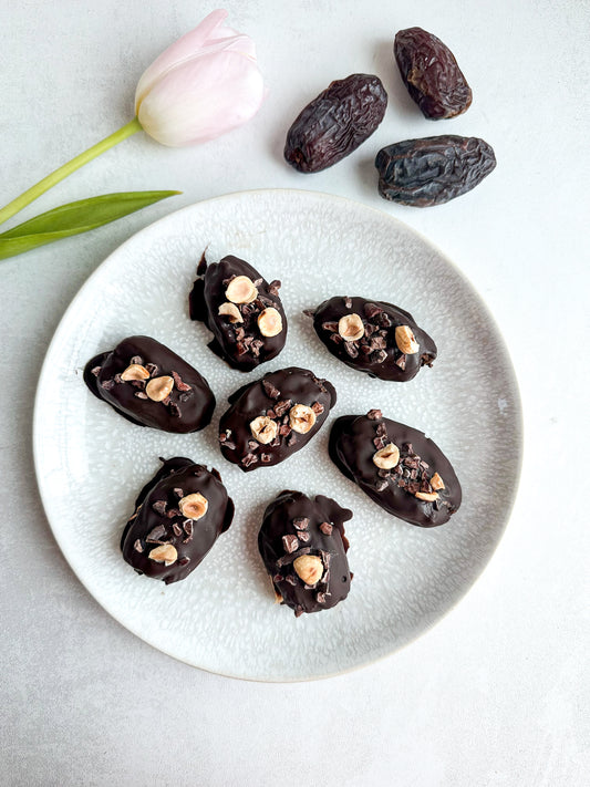sweet and salty nut butter stuffed medjool dates covered with dark chocolate, cacao nibs and hazelnuts.
