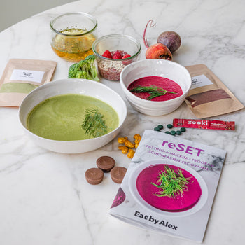 Health and wellness products including bowls of soup, a book titled 'reSET', and various items on a marble surface.